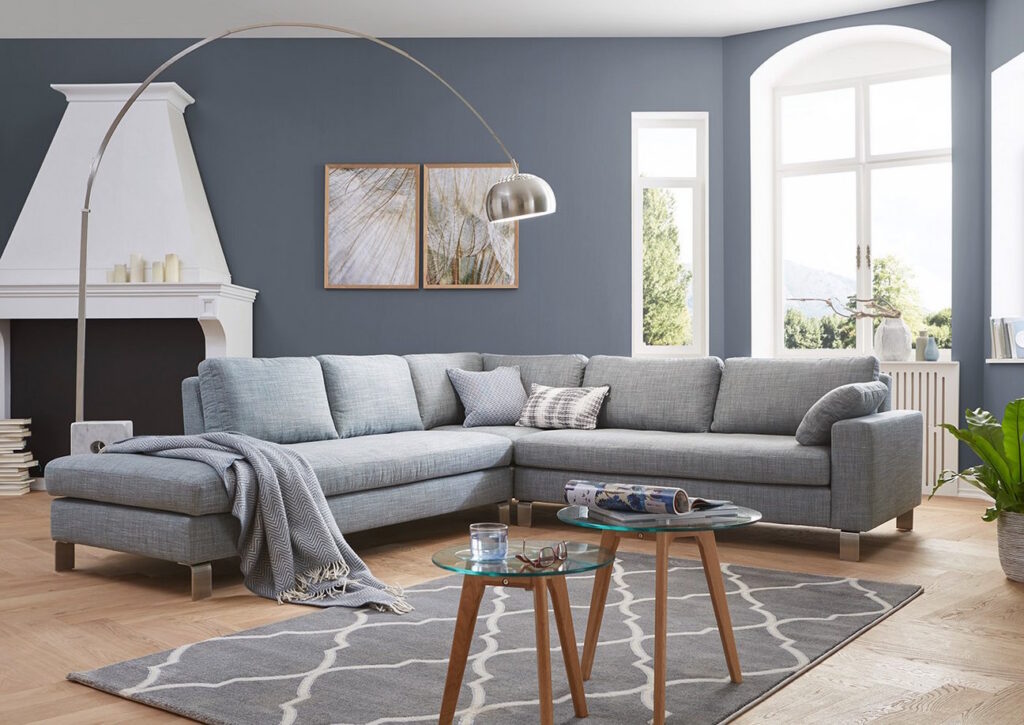 Große hellblaue Polsterecke mit Stoffbezug in einem modernen Wohnzimmer mit grauer Wand, Kamin und zwei runden Beistelltischen auf einem gemusterten Teppich